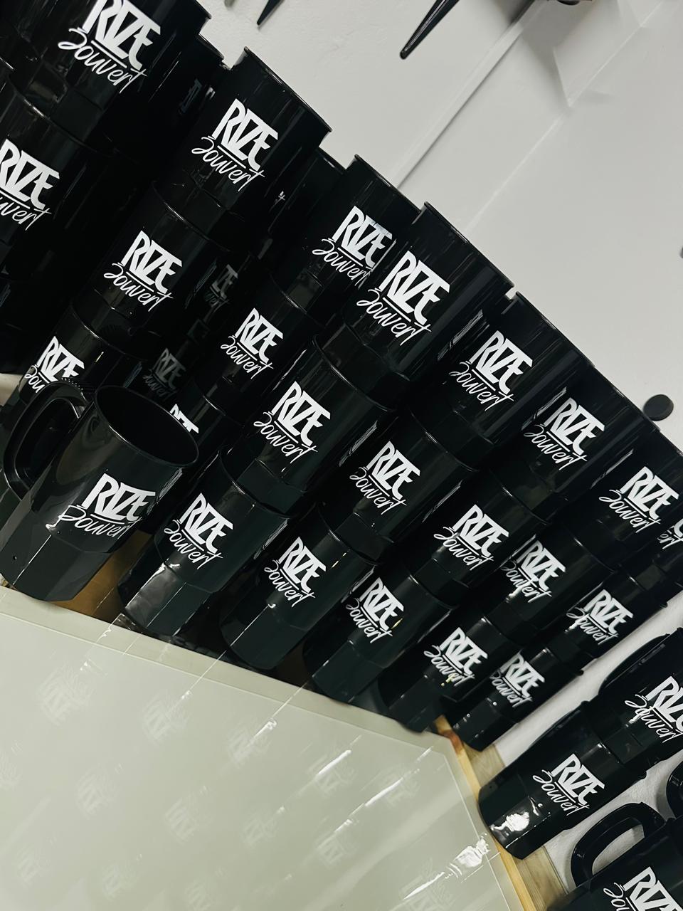 Rows of glossy black mugs with white stylised business lettering.