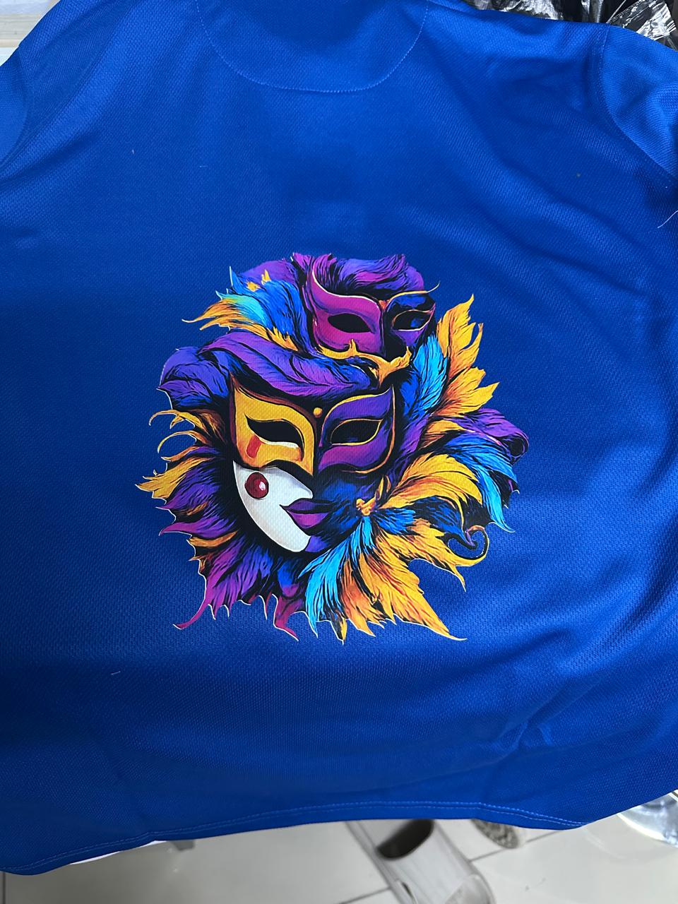 Blue garment carrying a vivid purple, yellow and cyan carnival mask illustration.