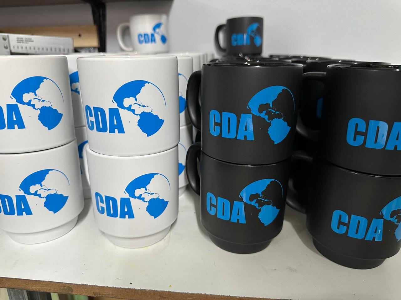 Black and white mugs carrying blue CDA lettering and a globe illustration.