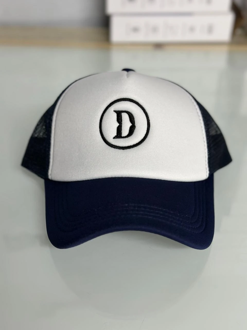 Navy and white cap with a black embroidered circular D emblem.