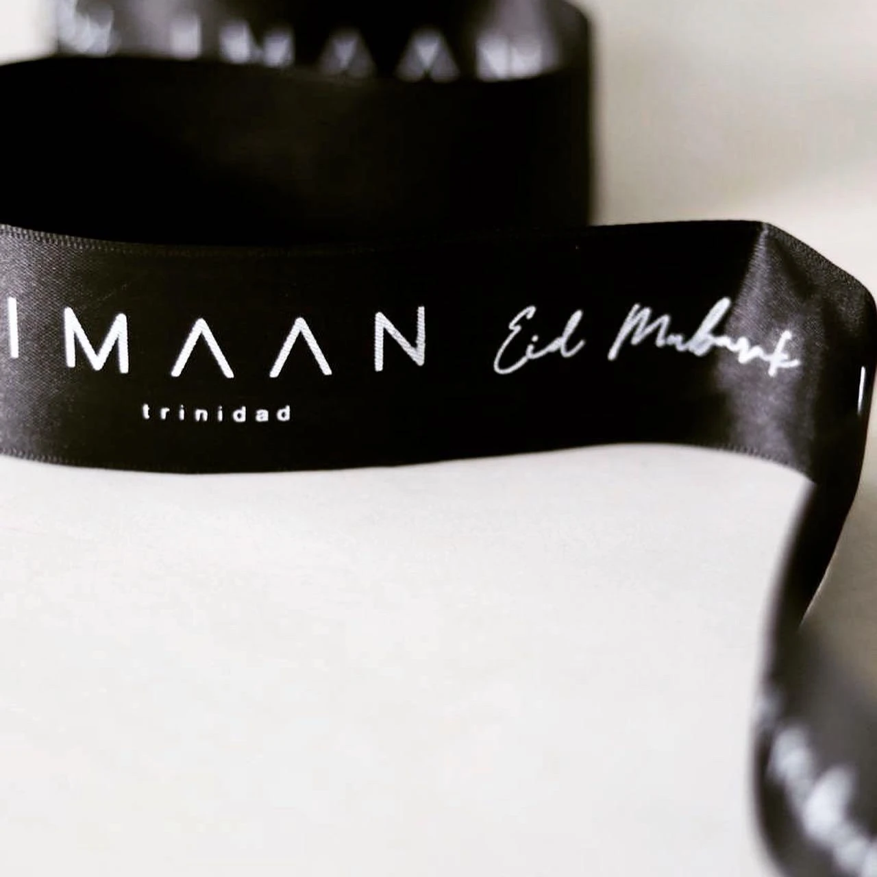 Black ribbon carrying white Imaan Trinidad and Eid Mubarak lettering.